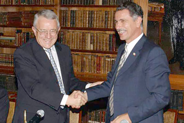 Two men shake hands in front of bookshelves